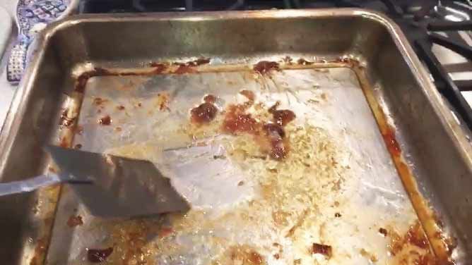 A spatula scrapping off drippings in a baking dish