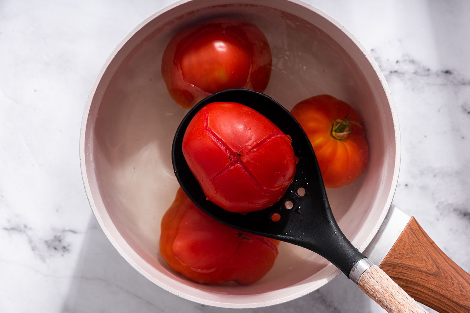 Slotted spoon removing blanched tomatoes from a pot of boiling water for bruschetta recipe