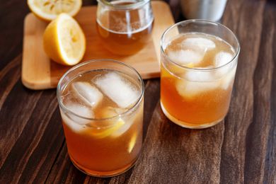 Two Gold rush cocktails with ice on a wood background.