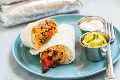 A plate of black bean, corn, and pepper freezer burritos with guacamole and sour cream on the side.