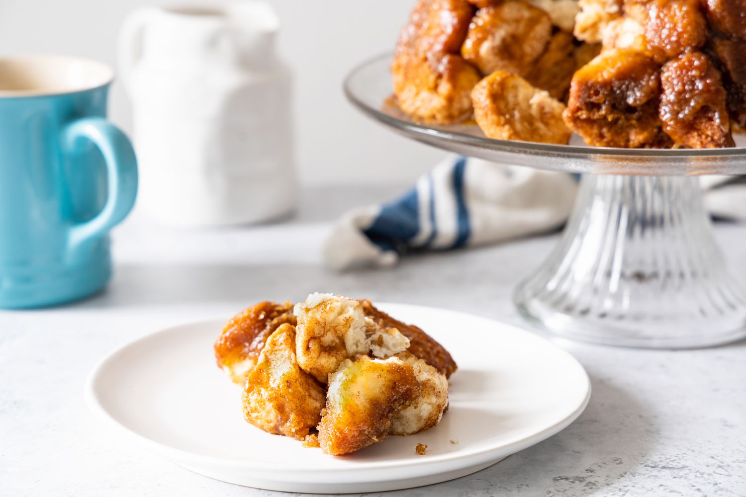 Plate of Monkey Bread Pieces, and in the Background, More on a Cake Stand and a Mug on the Counter 
