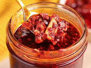 Spoonful of Homemade Chili Crispy Raised from Mason Jar With More Crisp, and in the Background, a Saucer With More Chili Crisp and a Kitchen Towel