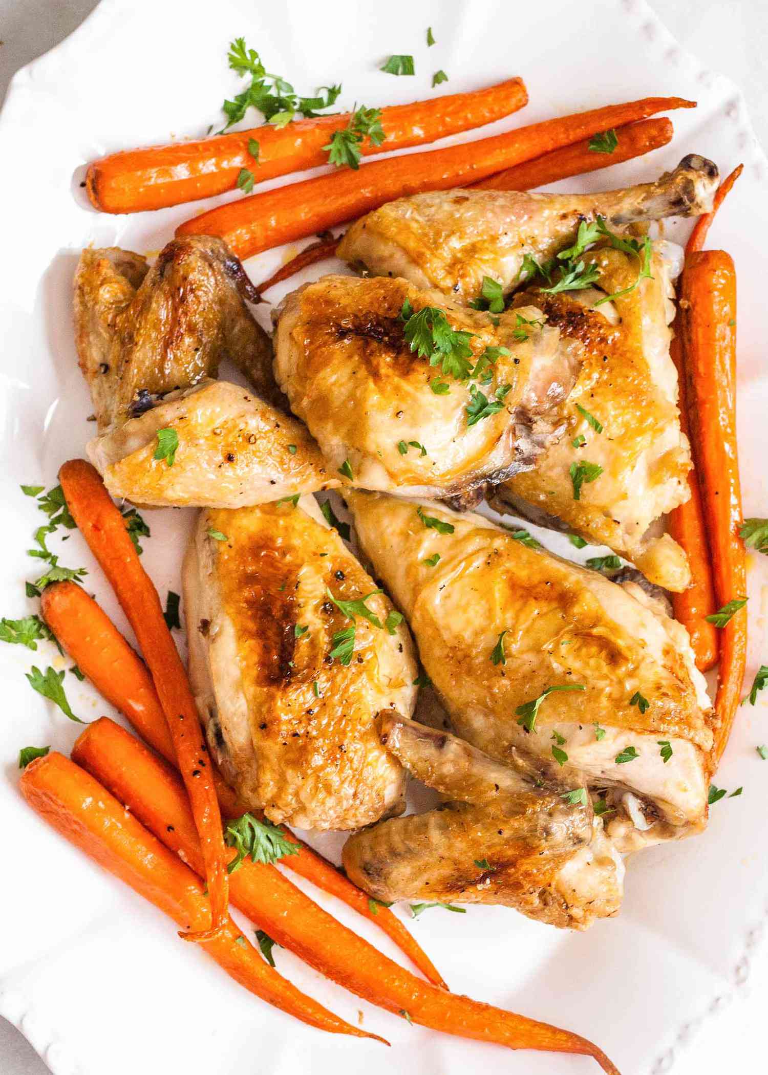 How to Make Chicken in the Oven Chicken cooked with carrots and herbs on white plate