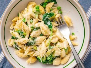 A bowl of creamy pasta with peas and spinach, garnished with cheese and accompanied by a fork