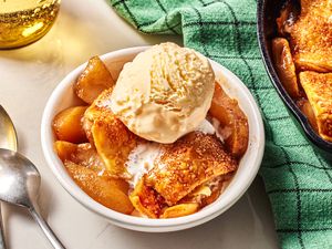 A white bowl with a serving of Apple Pandowdy topped with a scoop of vanilla ice cream