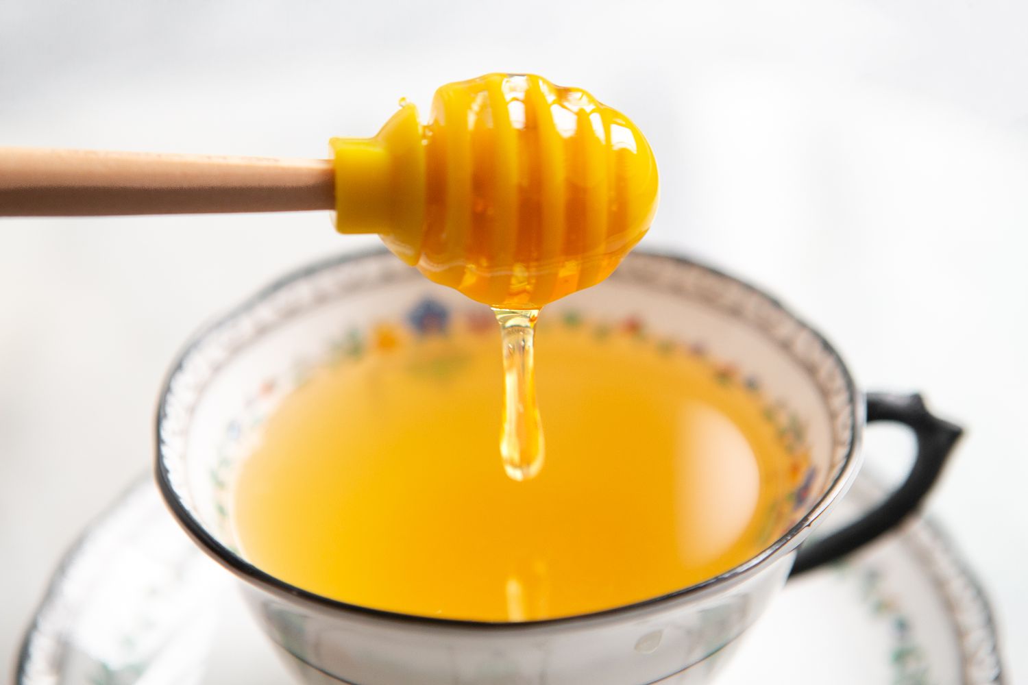 Honey Dipper With Honey Slowly Dripping Into a Teacup of Honey and Lemon Tea 
