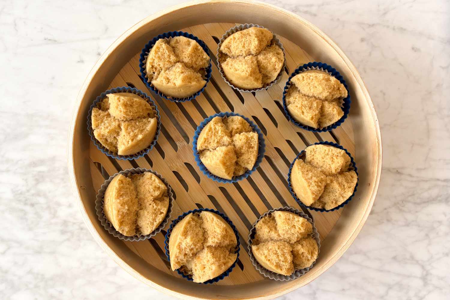 Overhead photo of a bamboo steamer with several prosperity cakes inside showing how the cakes split on top to resemble a bloom once steamed