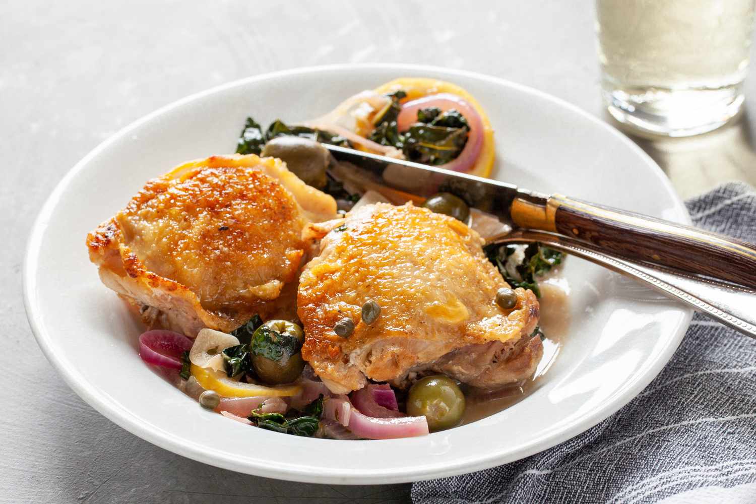 Chicken thighs on plate with olives, capers, and red onions. 