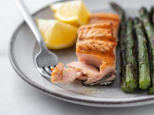 Grilled salmon with a forkful taken out alongside asparagus and lemon on the plate.