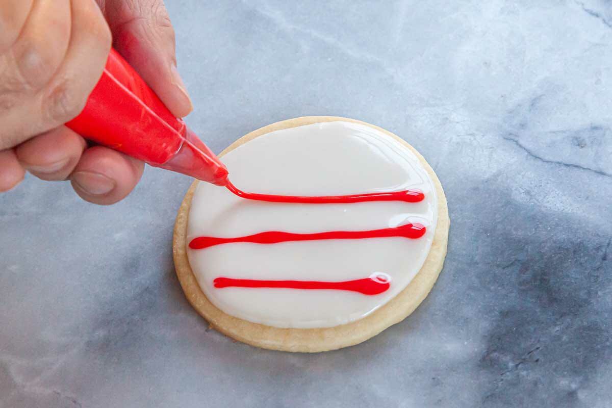 Red royal icing for sugar cookies is being piped over top white royal icing.