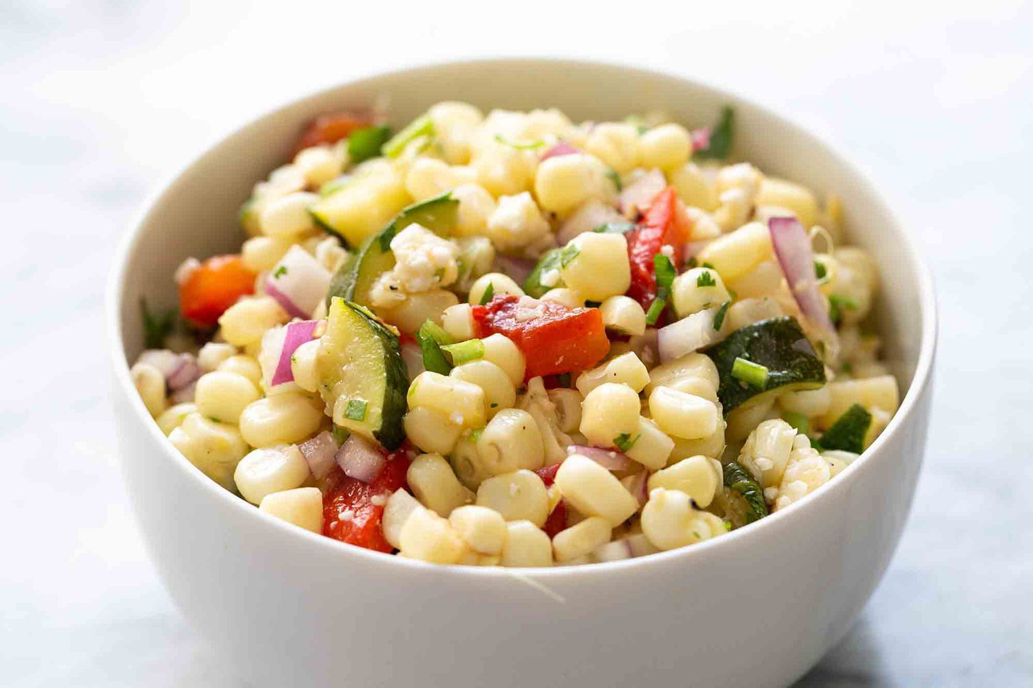 corn salad with zucchini and red bell pepper in white bowl