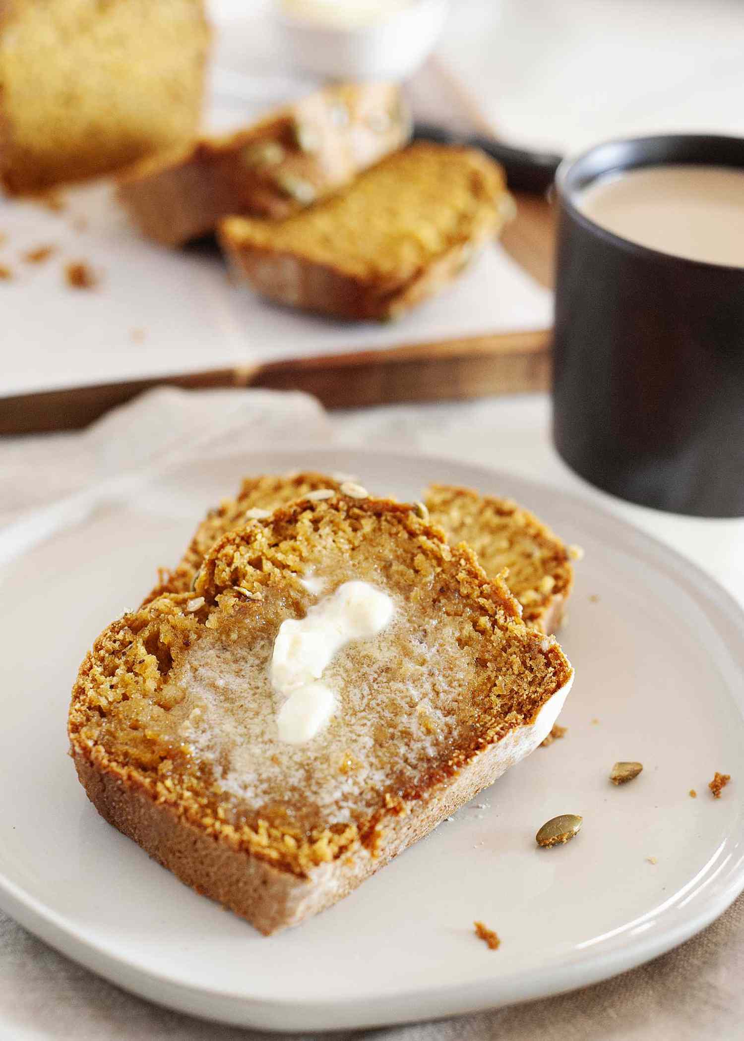 Two slices of the Best Vegan Pumpkin Bread on a white plate with butter melting on top.