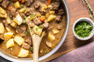 Pot of Easy Beef Stew with a Wooden Spatula, a Small Bowl of Parsley, a Sprig of Thyme, and a Kitchen Towel