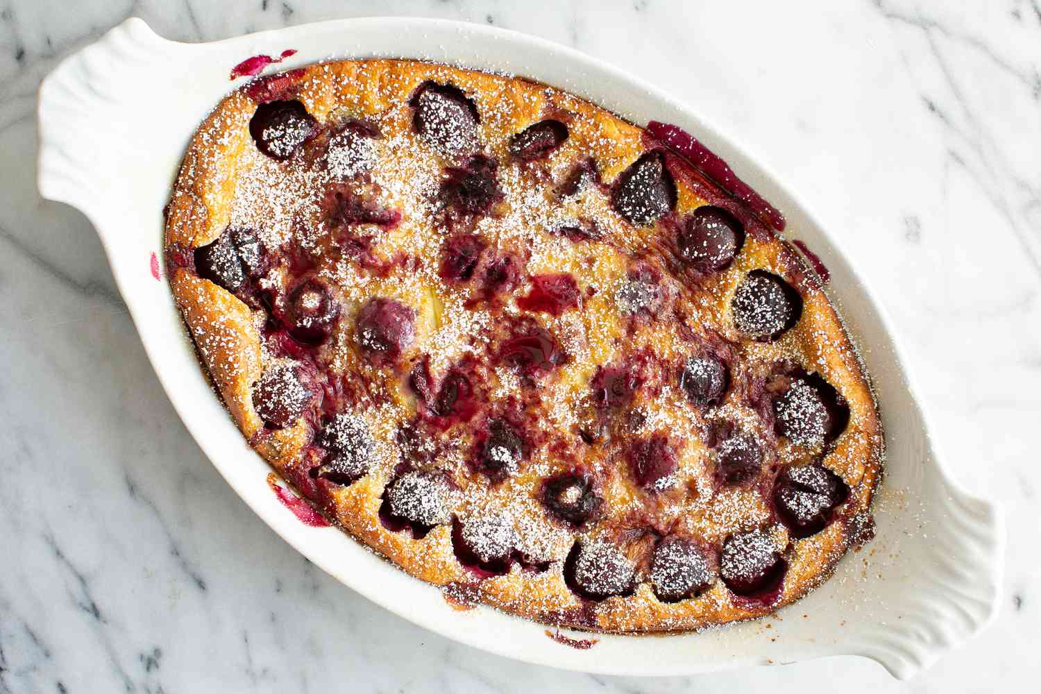Cherry Clafouti Dusted With Powdered Sugar in a White Baking Dish