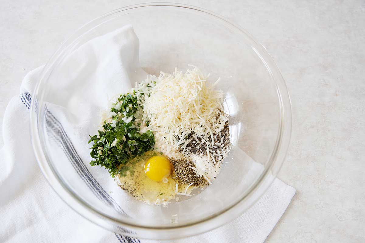 Eggs, breadcrumbs, herbs and cheese in a bowl.