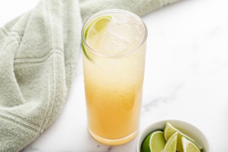 A tall glass of ginger ale soda with a bowl of sliced limes next to it.
