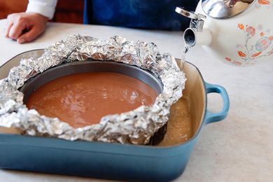 Chocolate cheesecake in waterbath. Person holding tea kettle with water to illustrate how to save a cheesecake if it gets wet.