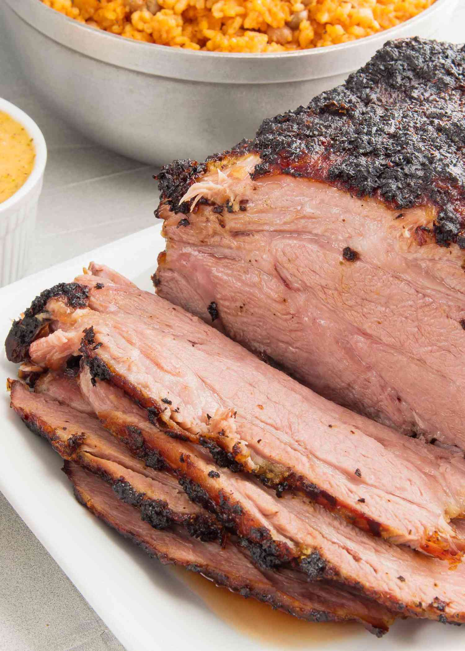 Roasted mojo marinated pork roast sliced on a white platter with a bowl of red rice on the side.