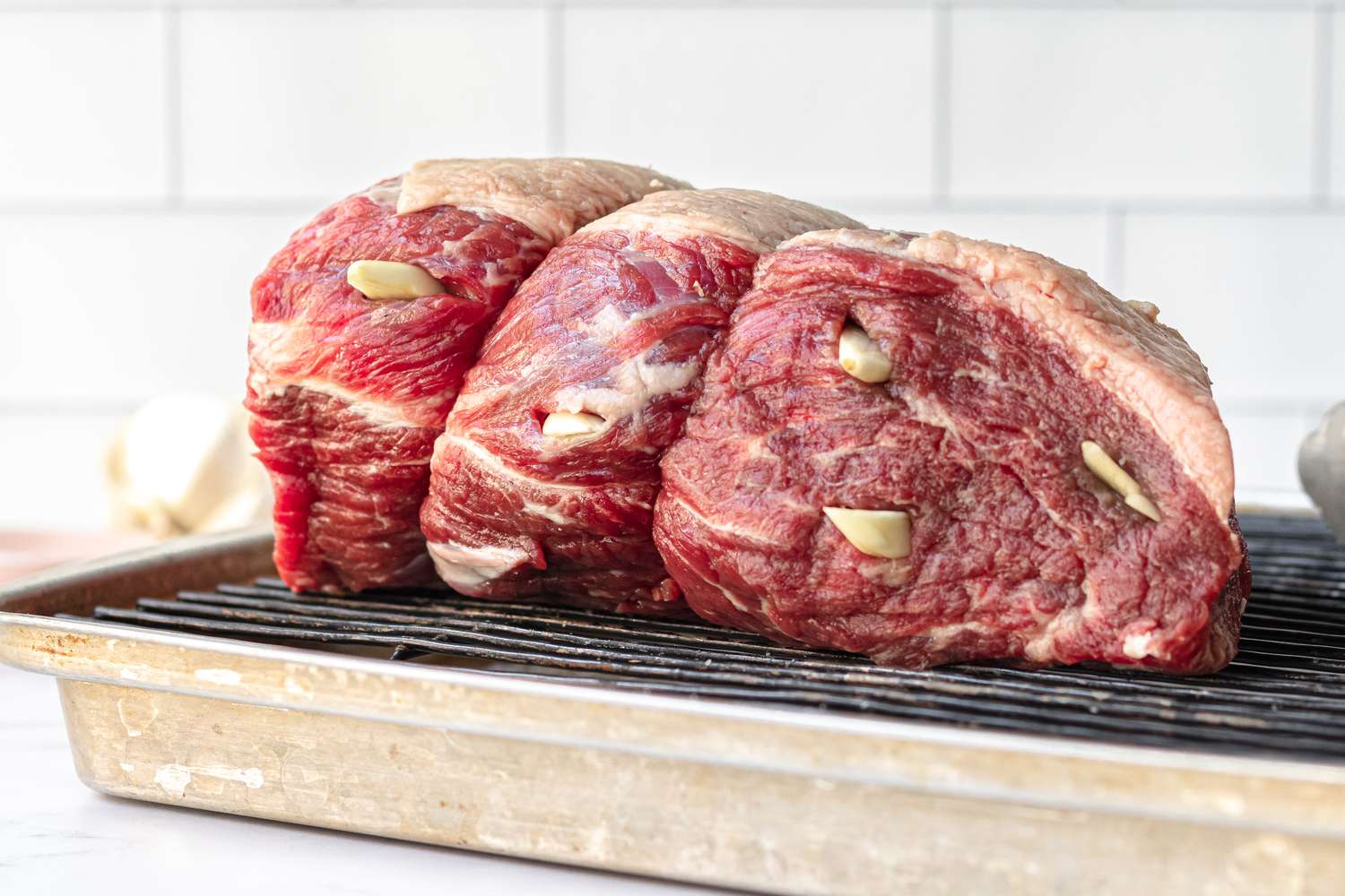 Side view of a baking tray with a rump roast set on a rack to make a roast beef recipe.