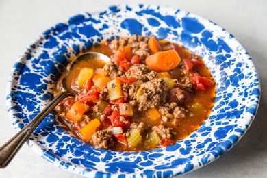 Hamburger soup with vegetables resting in a blue bowl 