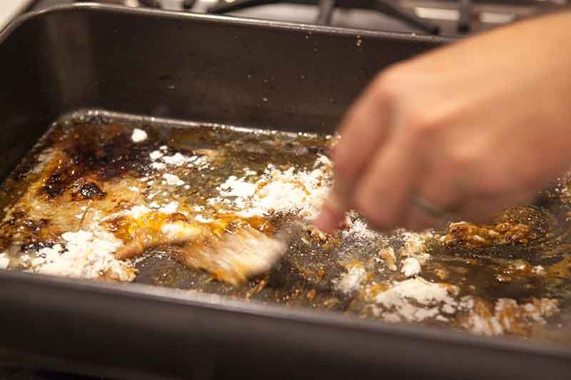 A spatula scraping off the turkey drippings and fat and mixing it with flour 