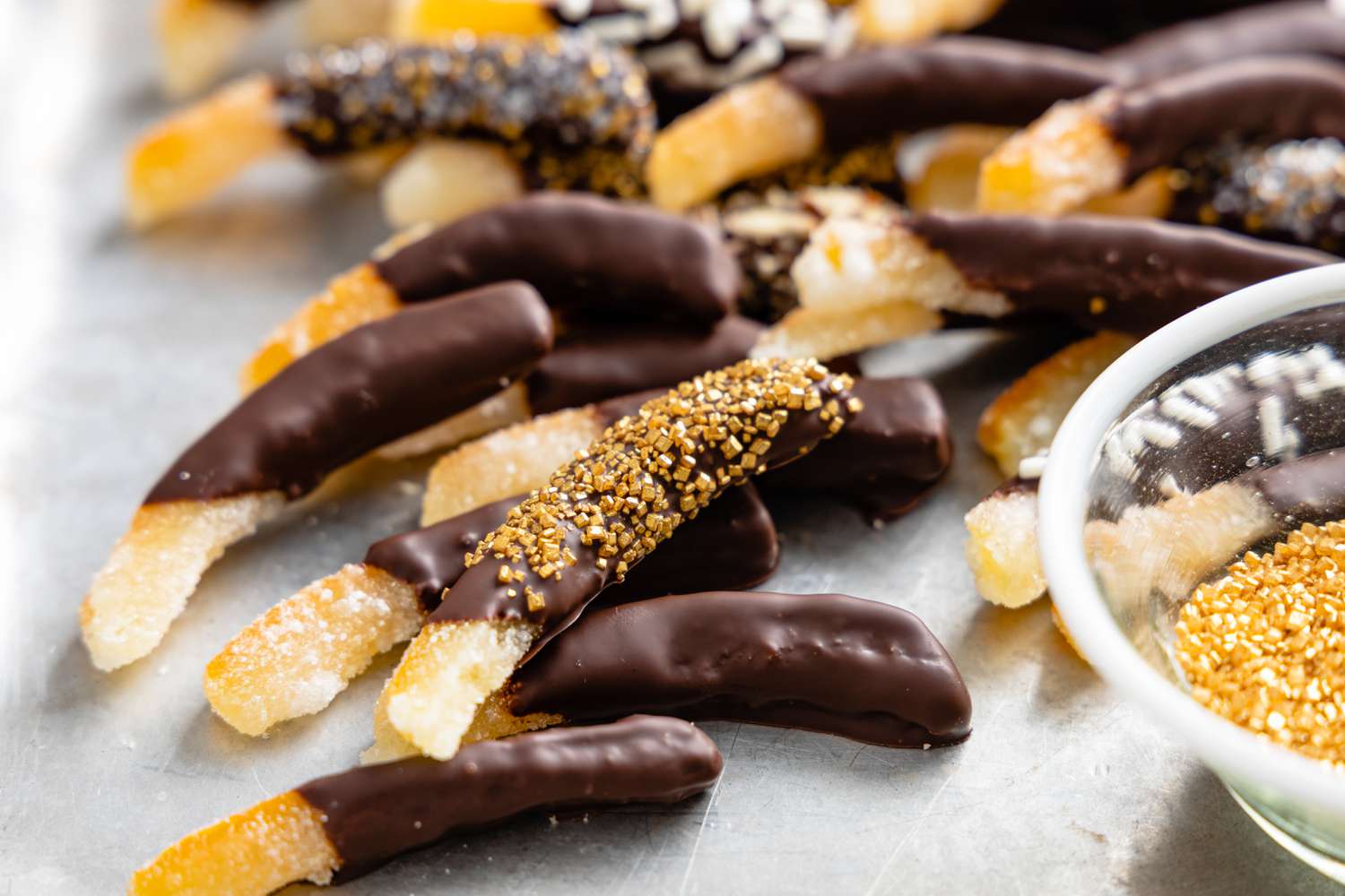 Chocolate Covered Orange Peels with Some Covered in Sprinkles Next to a Bowl of More Sprinkles