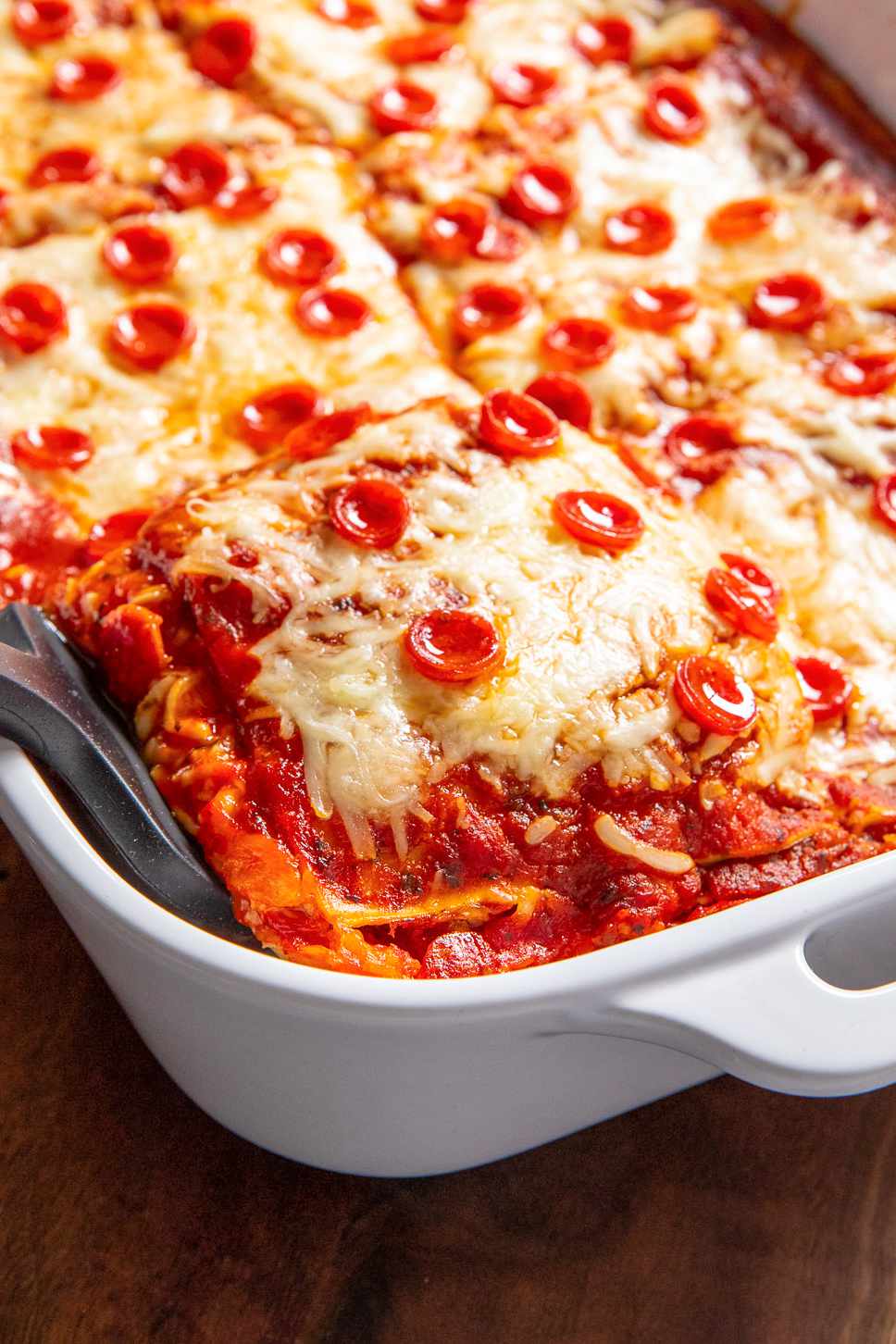 Spatula Slightly Lifting a Slice of Pepperoni Pizza Lasagna From a Casserole Dish With the Rest of the Lasagna