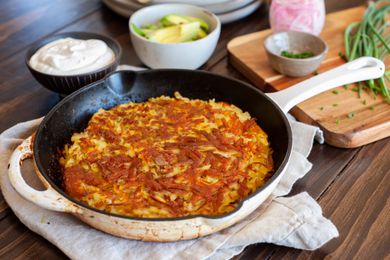 Slice of Rosti on a Plate with Bacon, Sour Cream, Sliced Avocados, and Sliced Onions