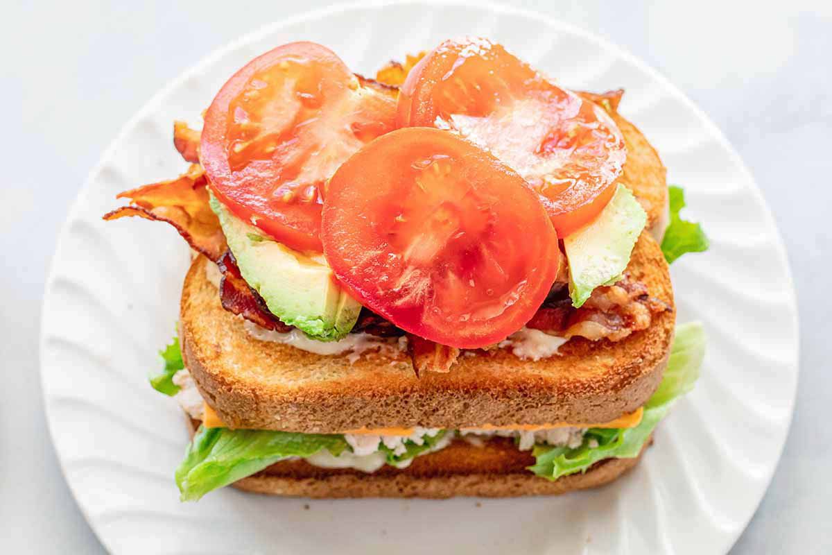 Homemade turkey club with two pieced of bread and tomato, bacon and avocado stacked on top of the toasted bread.