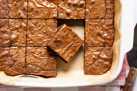 Overhead view of a white baking dish of 3-ingredient brownies on parchment paper, sliced into squares with one slice removed