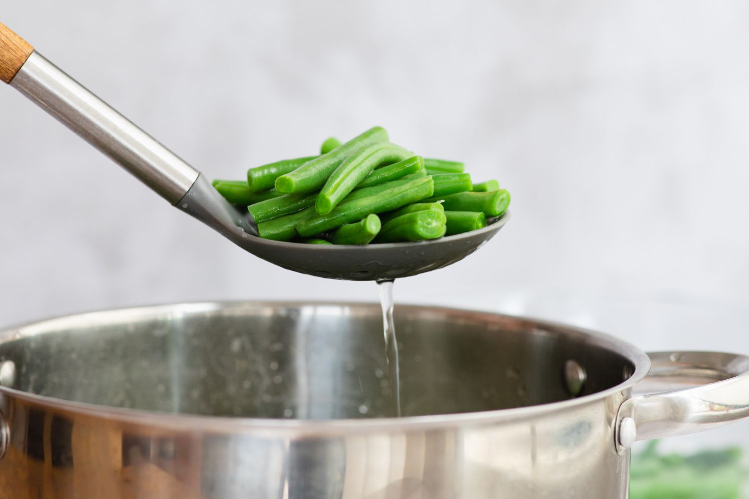 A slotted spoon with blanched green beans to make green bean salad.