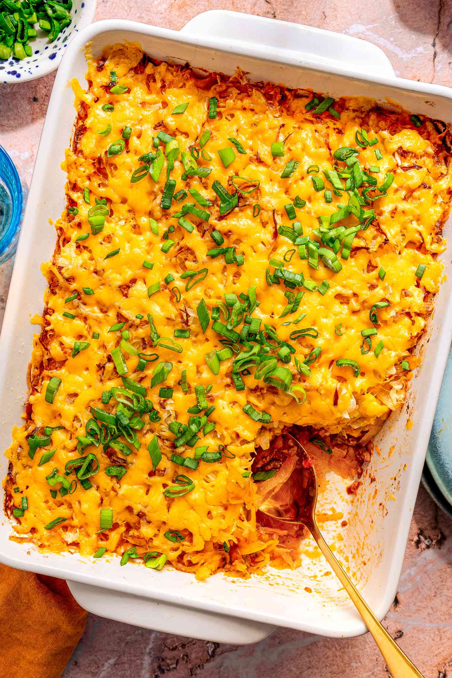 shipwreck casserole in a casserole dish at a table setting with a bowl of scallions, plate, and glass of water 