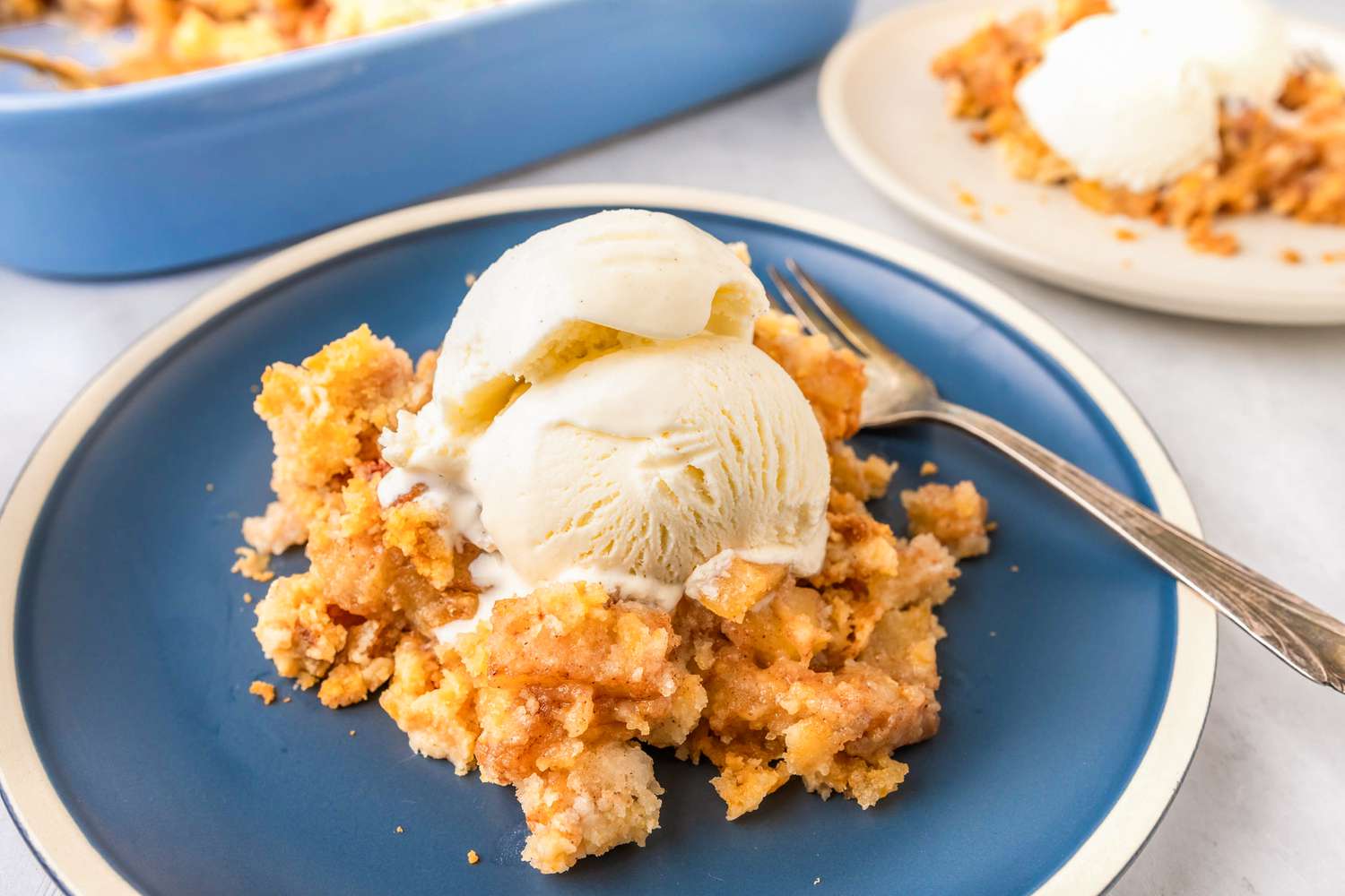 A serving of apple dump cake topped with a scoop of vanilla ice cream on a white rimmed blue plate