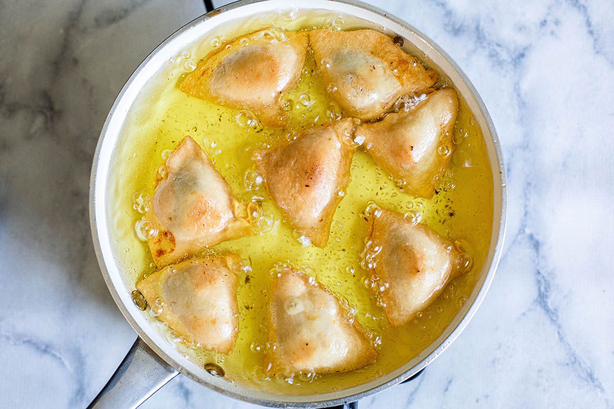 Pot of oil with samosas being fried.