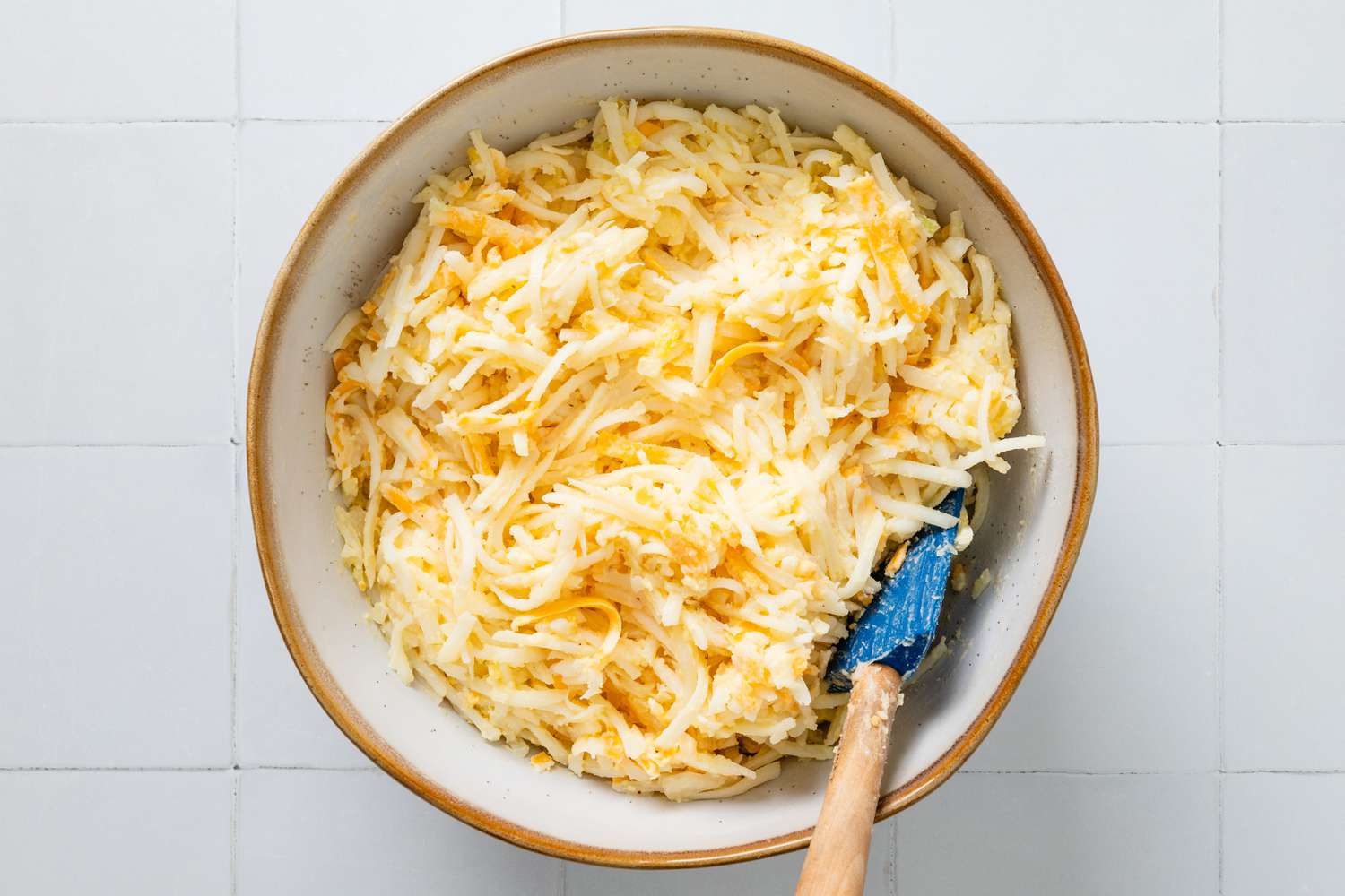 Copycat Cracker Barrel hash brown casserole mixture in a bowl with a rubber spatula