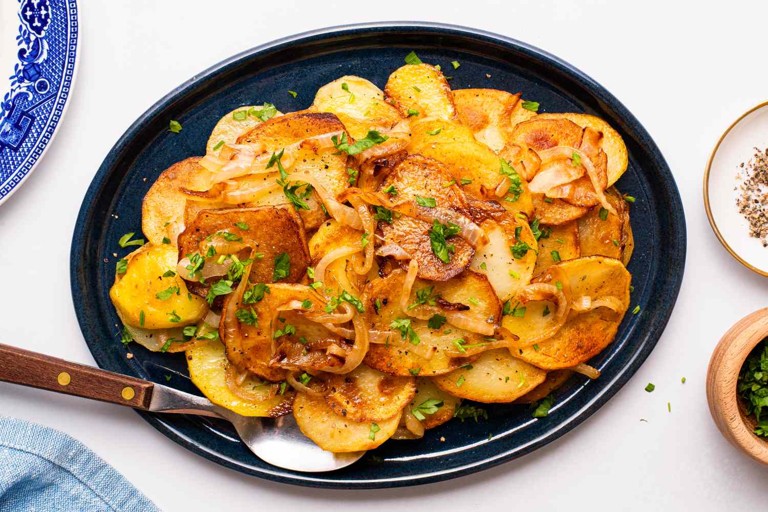 Lyonnaise potatoes on a platter at a tablet setting with a small plate of crushed peppers, bowl of minced parsley, and a plate 