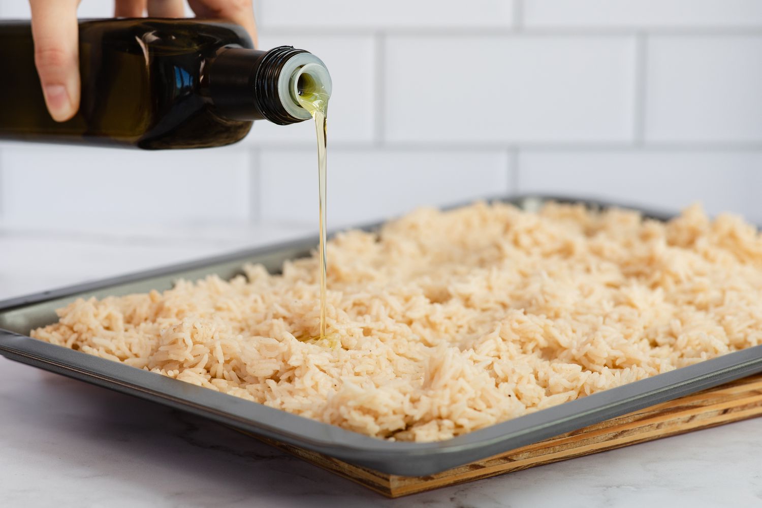 Adding olive oil to a sheet pan of rice to make a dirty rice recipe.
