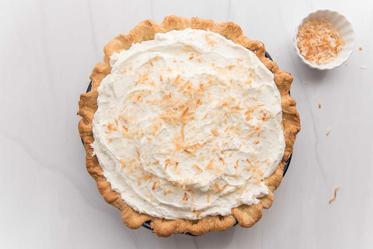 Overhead view of a homemade coconut cream pie with a small container of toasted coconut to the right.