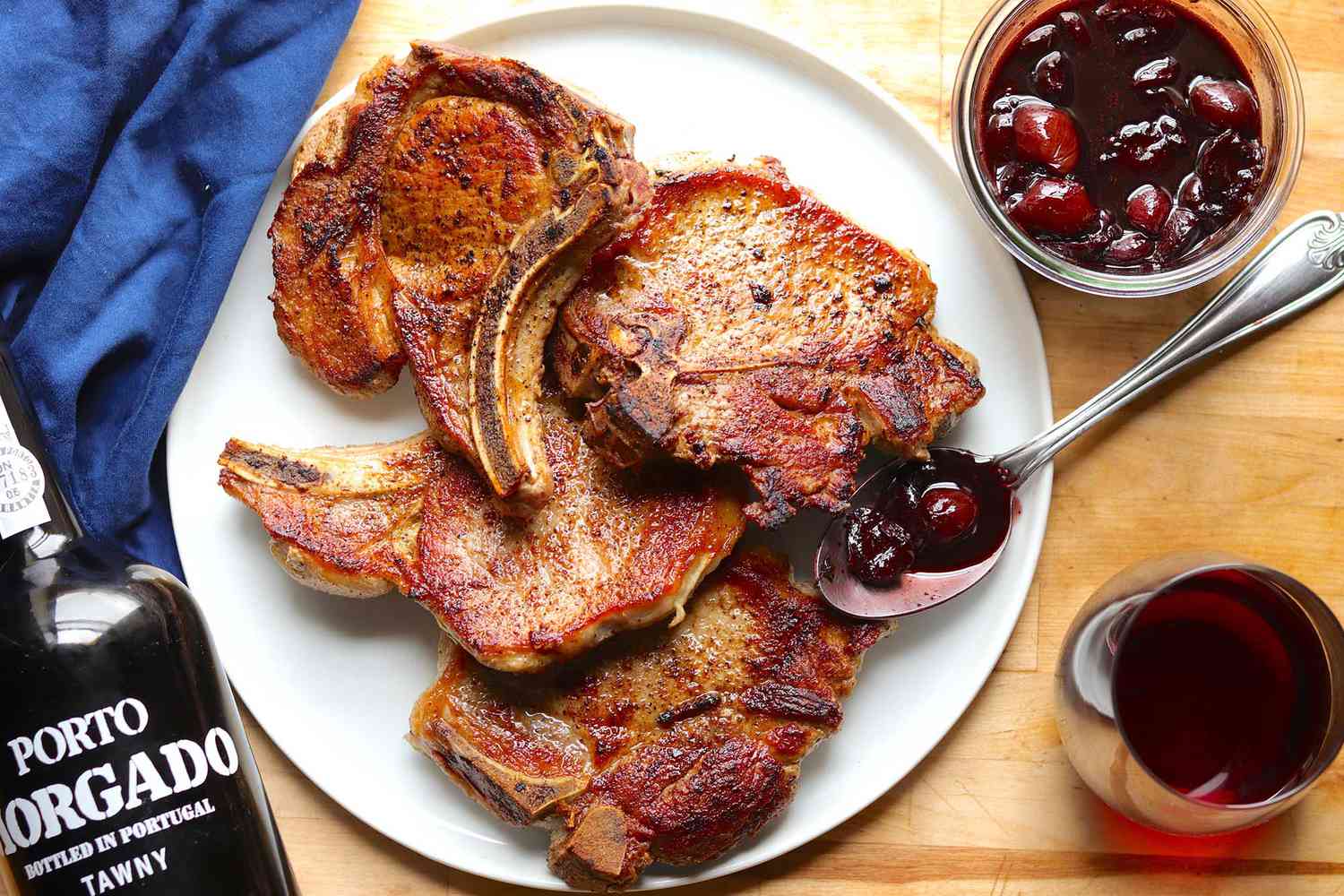 A platter of pan fried pork chops with a small bowl of cherry sauce on the side.