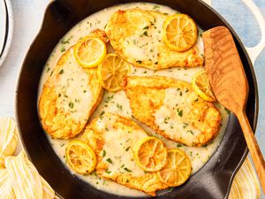 Chicken Francese in a skillet with a wooden spatula