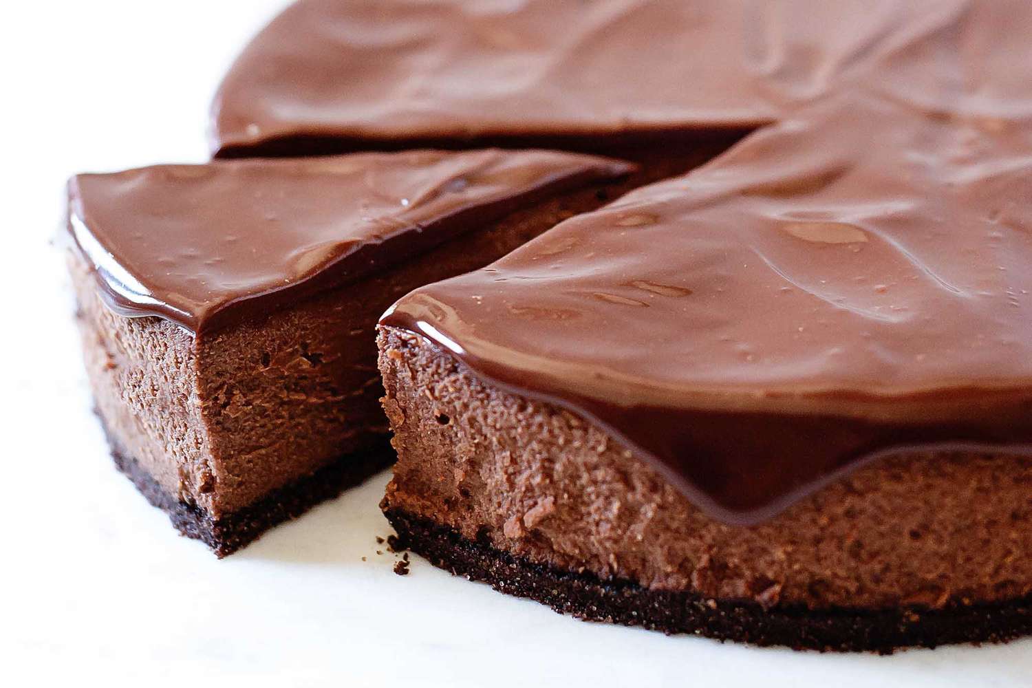 Close up of the best chocolate cheeescake with dripping ganache frosting on a white background.