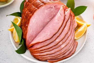 Spiral cut cooked ham on a platter with lemon slices and leaves all on a quartz countertop