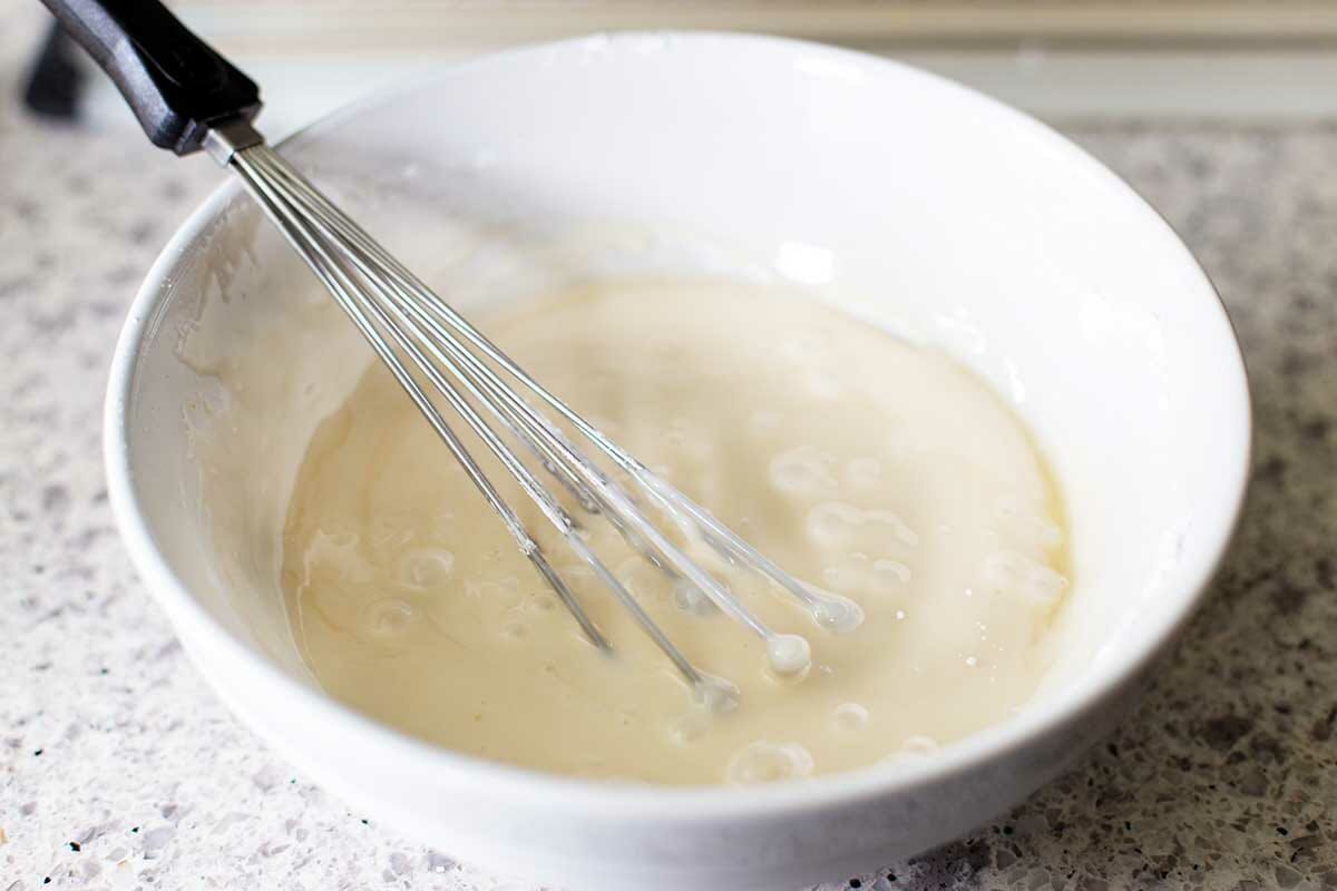 Glaze is whisked in a white bowl for Hungarian Nut Horns.