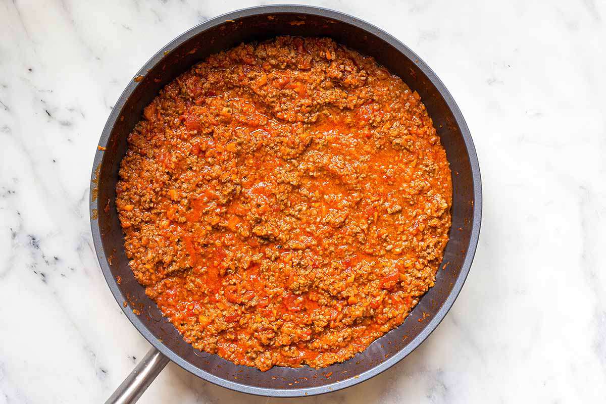 A homemade bolognese sauce in a skillet on a marble countertop