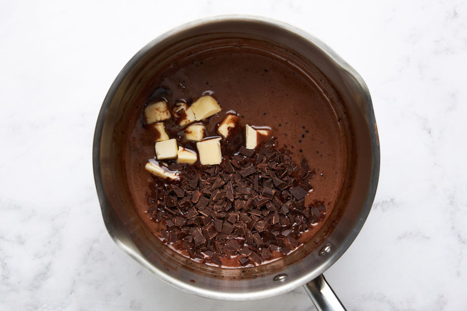 Butter and chopped choclate added to the saucepan with the base ingredients for hot fudge sauce recipe