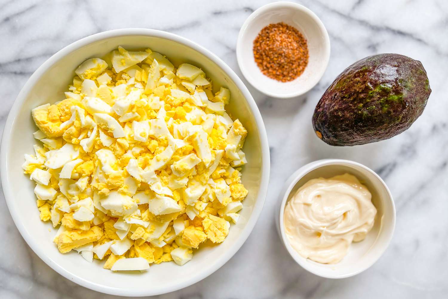 egg salad ingredients: bowl of chopped eggs, bowl of Tajin, an avocado (not cut), and a bowl of mayo