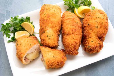Homemade Chicken Cordon Bleu on a white platter with lemon wedges.