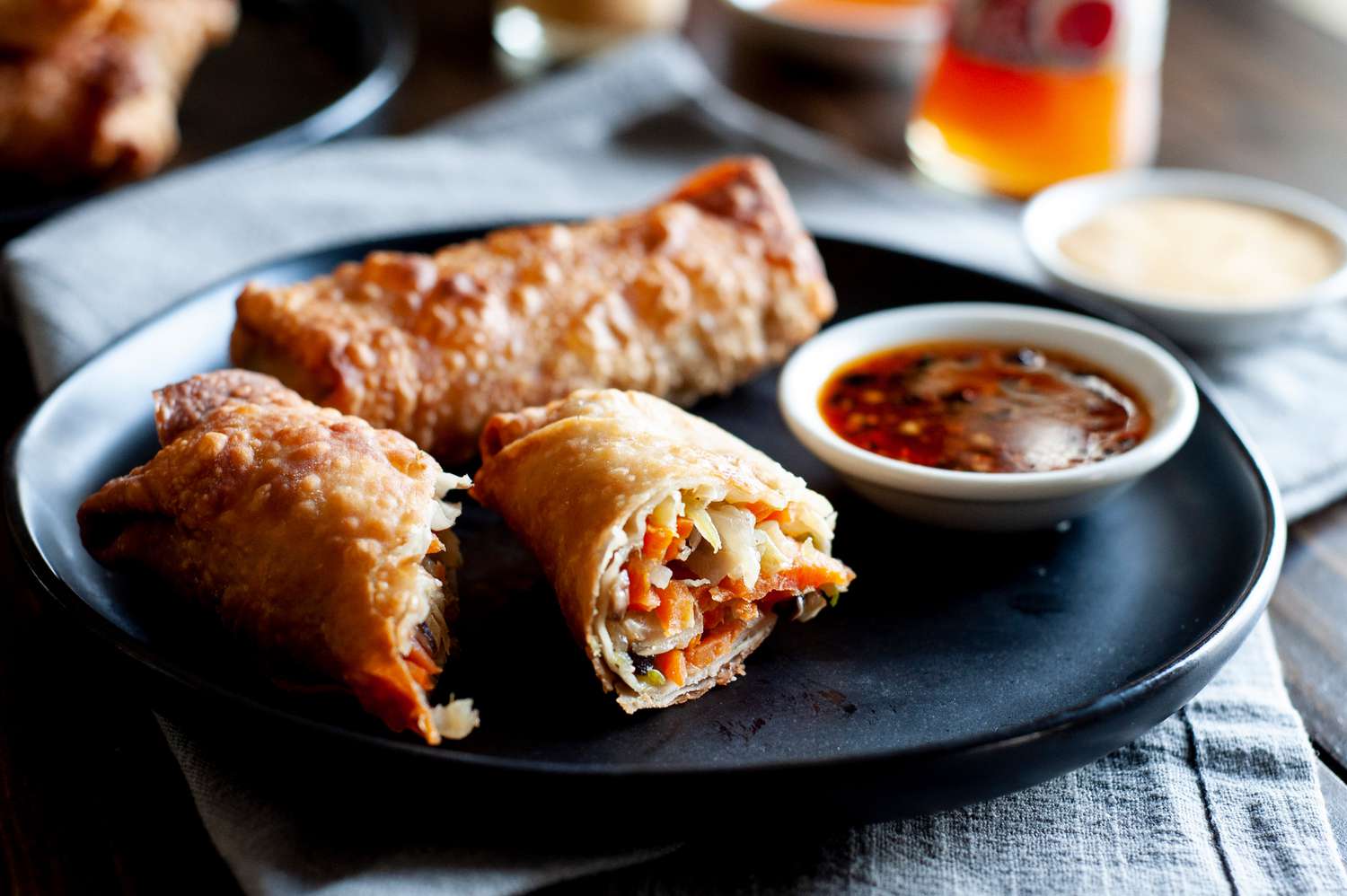A dark plate with stacked vegetable egg rolls and dipping sauce