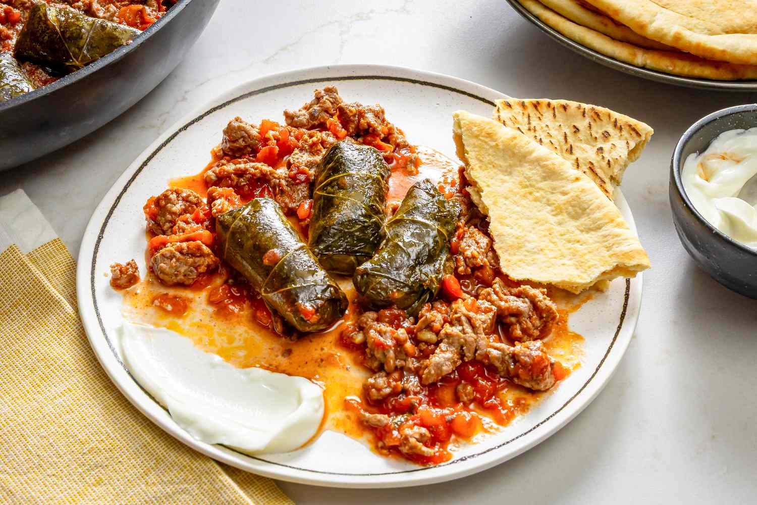 Dolmas served with ground beef, pita bread, and yogurt on a plate