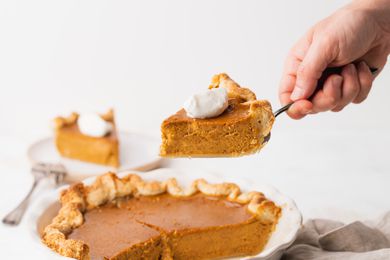 Slice of Old Fashioned Pumpkin Pie Held on a Pie Server with the Rest in a Pie Dish Below It 